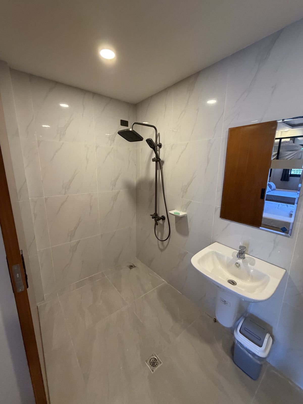 A marble-tiled bathroom with a rain shower head, basin and mirror