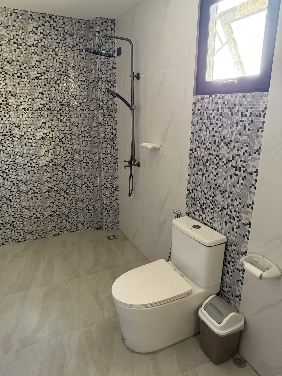 A rain shower against a mosaic feature wall in a second bathroom