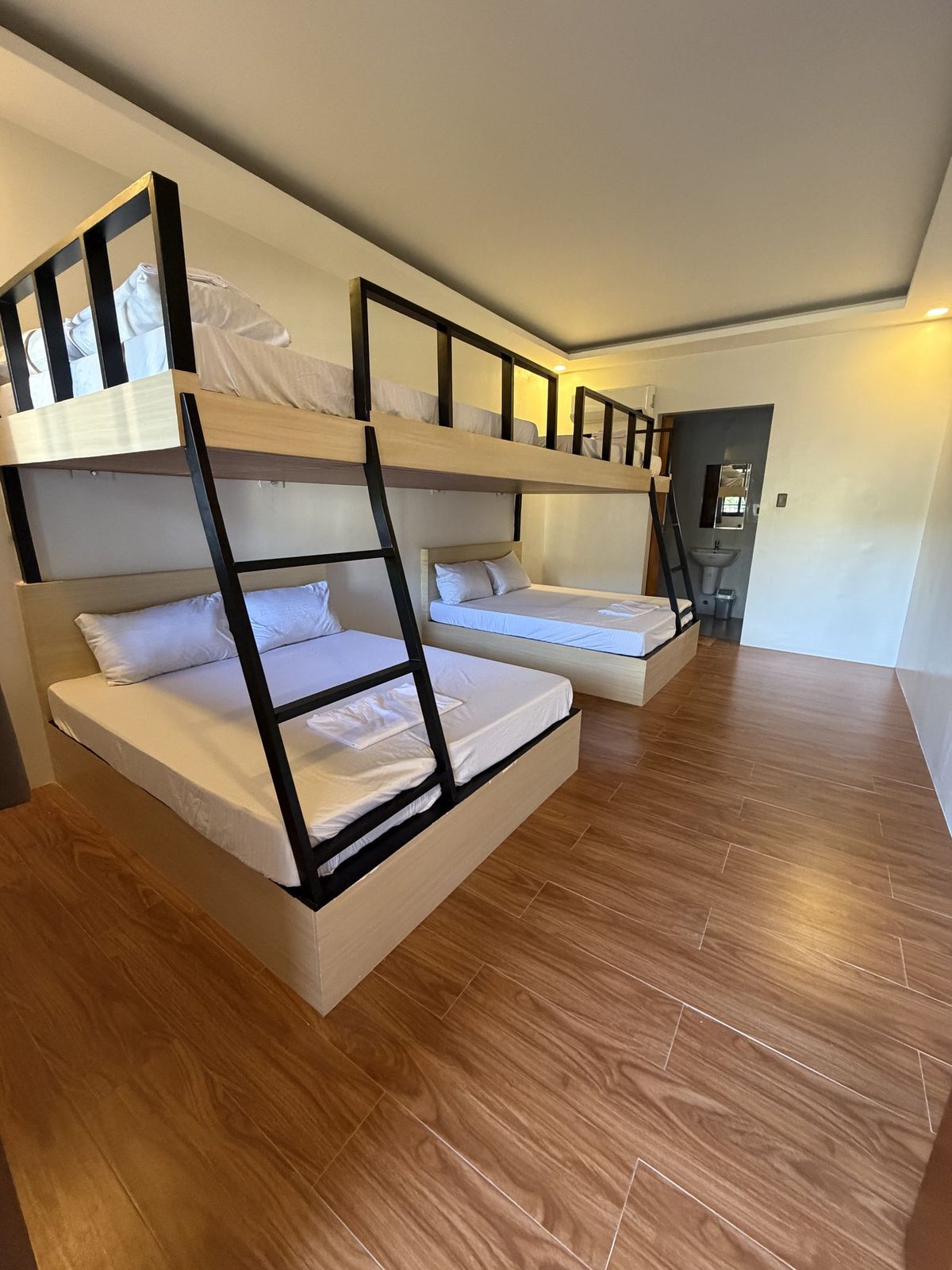 Two sets of black steel bunk beds on a wood floor, made up and ready